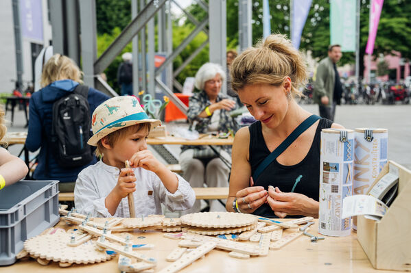 Ein Kind baut gemeinsam mit einer weiblich gelesenen Person mit Holzteilen.