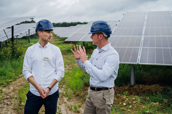 Zwei Männer unterhalten sich vor PV-Modulen auf einer Agrarfläche.