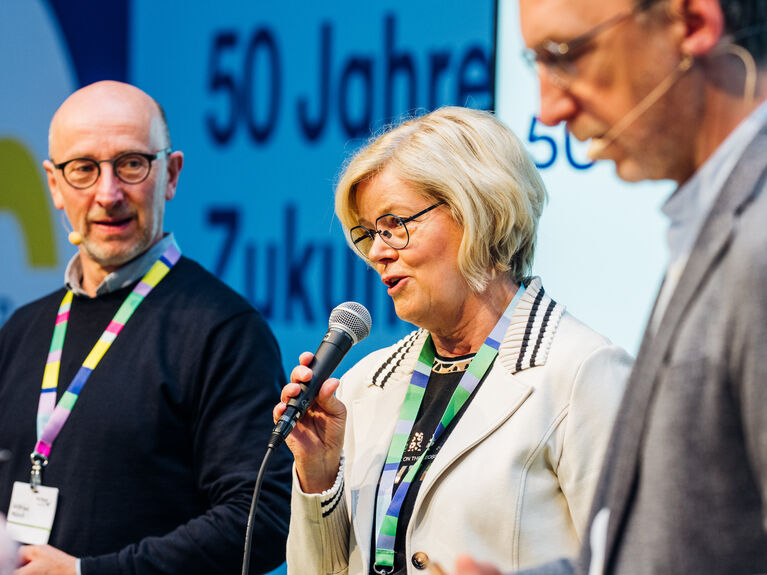Das Bild zeigt Christina Optz im Gespräch mit Wilfried Münch und dem Moderator einer Veranstaltung.
