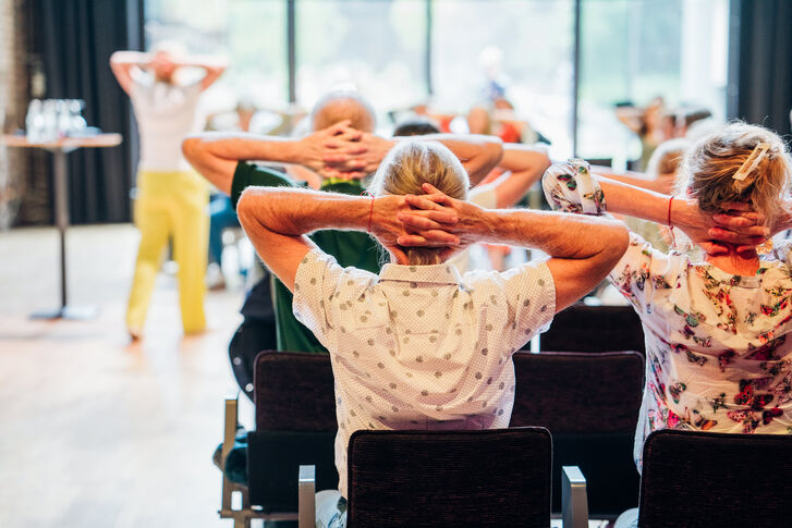 Das Bild zeigt eine Gruppe von Menschen bei Dehnübungen im Sitzen.