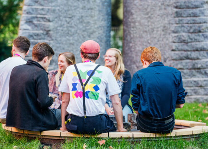 Sechs Personen sitzen im Garten der GLS Bank im Kreis zusammen.