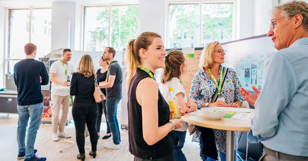 Das Bild zeigt Menschen im Werkraum der GLS Bank im Austausch an Stehtischen.