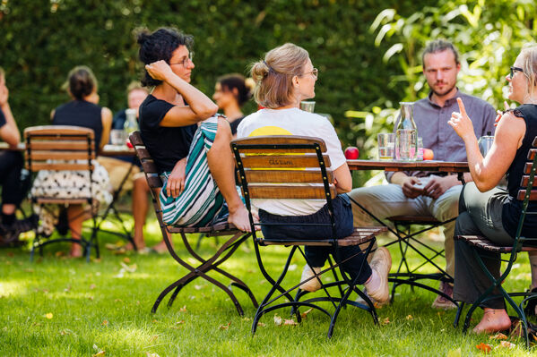 Das Bild zeigt Menschen an einem Tisch im Garten des GLS Bank Hauptsitzes in Bochum.