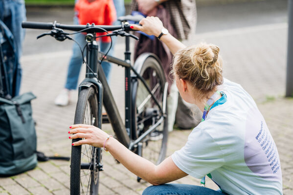 Eine Frau ist von hinten zu sehen, wie sie den Reifendruck bei einem Fahrrad prüft.