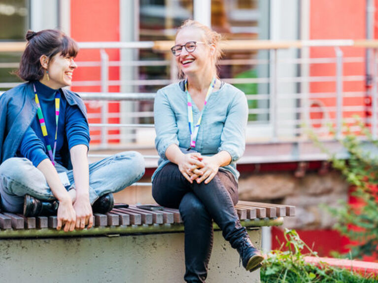 Zwei Frauen sitzen lachend im Garten der GLS Bank.