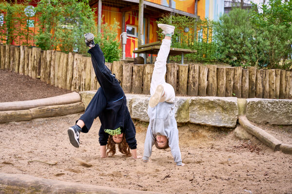 Zwei Kinder machen Handstand in einem Sandkasten auf der Außenfläche einer Schule.