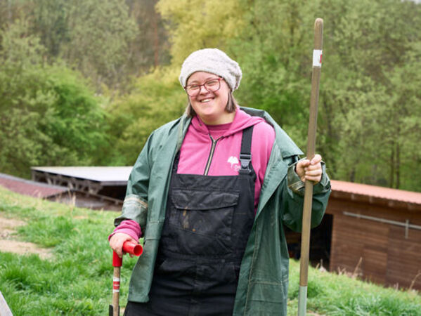 gls-bank-nachhaltigkeitsbericht-2023-deepdive-soziales-gesundheit-selbstbestimmung Eine Frau steht lächelnd im Garten und hält ein Gartengerät fest.